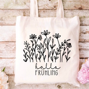 May include: A white tote bag with a black line drawing of flowers and the text "hallo fr&uuml;hling" on it.