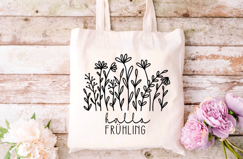 May include: A white tote bag with a black line drawing of flowers and the text "hallo fr&uuml;hling" on it.