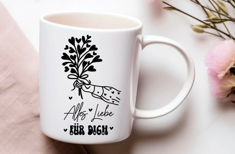 May include: White ceramic mug with a black and white illustration of a hand holding a bouquet of hearts. The text "Alles Liebe f&uuml;r Dich" is printed on the mug.