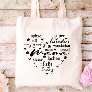 Może przedstawiać: Biała torba z pł&oacute;tna z czarnym tekstem, kt&oacute;ry brzmi "spitze super * toll einzigartig * besonders * wunderbar mutig liebevoll *Mama * klasse * lachen * Liebe lustig" z sercami i gwiazdami wok&oacute;ł tekstu.