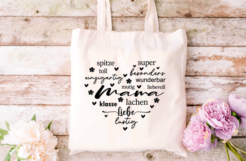 Może przedstawiać: Biała torba z pł&oacute;tna z czarnym tekstem, kt&oacute;ry brzmi "spitze super * toll einzigartig * besonders * wunderbar mutig liebevoll *Mama * klasse * lachen * Liebe lustig" z sercami i gwiazdami wok&oacute;ł tekstu.