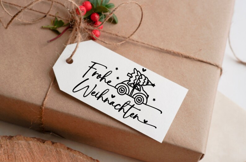 May include: A white gift tag with black text that says "Frohe Weihnachten" and a black and white illustration of a car carrying a Christmas tree.