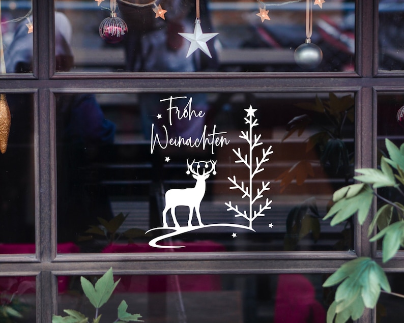 May include: A white vinyl sticker with a Christmas tree, reindeer, and the text "Frohe Weihnachten" on a shop window.