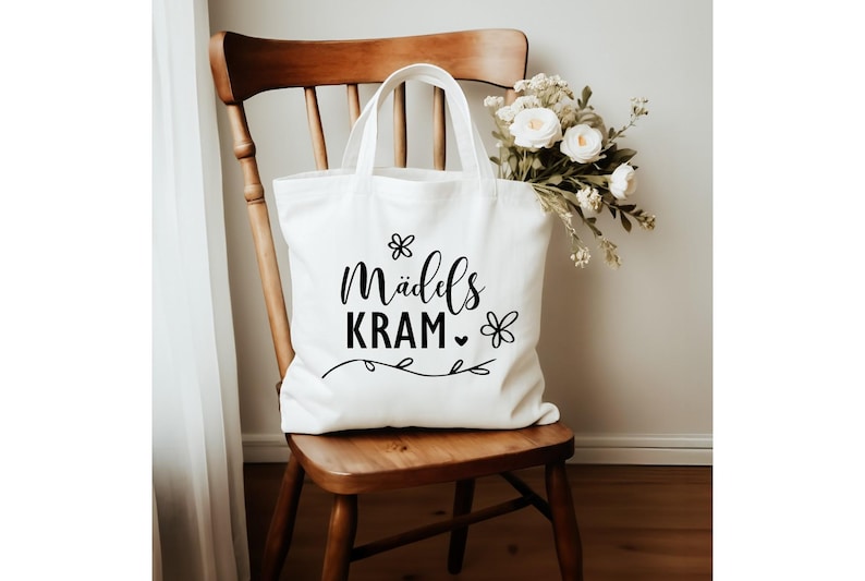 May include: White tote bag with black text that reads "M&auml;ddels Kram" with a small heart and flower designs.