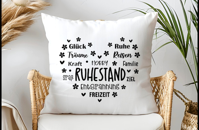 May include: White square throw pillow with a heart-shaped design in black. The design includes the word "RUHESTAND" and other words like "Gl&uuml;ck", "Tr&auml;ume", "Kraft", "HOBBY", "Spa&szlig;", "Entspannung", "Freizeit", "Ruhe", "Reisen", "Familie", and "Ziel".
