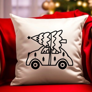 May include: White throw pillow with a black line drawing of a car carrying a Christmas tree on top. The car has small trees on the sides and a star on top of the tree.