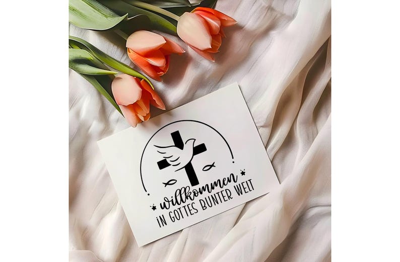 May include: A white card with a black cross, dove, and fish design, with the German text "Willkommen in Gottes bunter Welt." The card is placed on a white fabric with orange tulips.