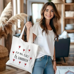 May include: White tote bag with a black and red design. The bag has the text "Bin mal kurz Wein kaufen" and several red wine glasses printed on it.