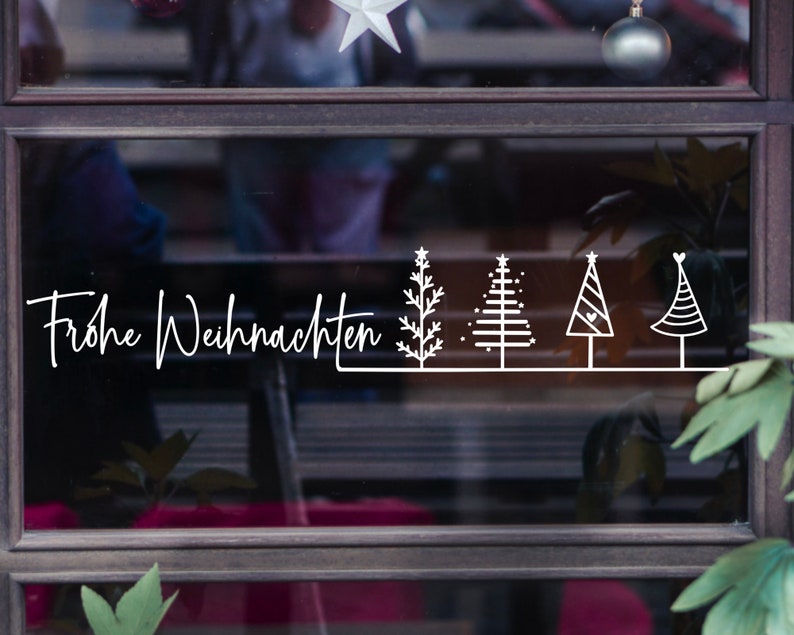 May include: A window with a white sign that says "Frohe Weihnachten" and five stylised Christmas trees.