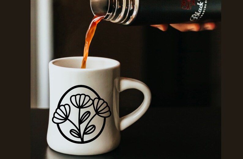 May include: A white ceramic mug with a black outline of a flower design. Coffee is being poured into the mug from a black thermos.