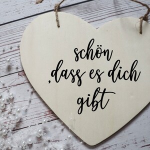 Puede incluir: Un letrero de madera blanco en forma de coraz&oacute;n con el texto "sch&ouml;n dass es dich gibt" en letras cursivas negras.