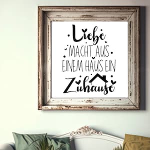 May include: A framed print with a white background and black text that reads "Liebe macht aus einem Haus ein Zuhause" which translates to "Love makes a house a home".