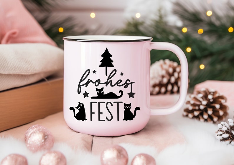 May include: A pink ceramic mug with a black handle and a black design of a Christmas tree, three cats, and the text "frohes FEST".
