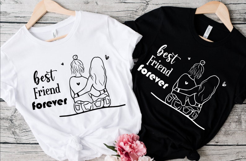 May include: Two white t-shirts with black text and a graphic of two girls hugging. The text on the shirts says "best friend forever".