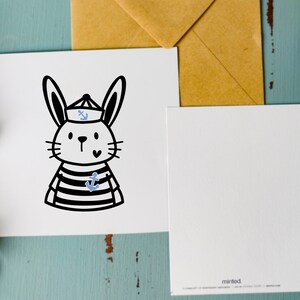 May include: A white card with a black and white illustration of a rabbit wearing a sailor hat with a blue anchor on it. The rabbit is wearing a striped shirt with a blue anchor on it. The card has a white envelope with the word "minted" printed on it.