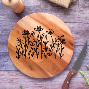 May include: A round wooden serving board with a black floral design. The board is made of acacia wood and has a natural finish.