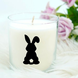 May include: A white candle in a clear glass jar with a black silhouette of a bunny rabbit on the front.