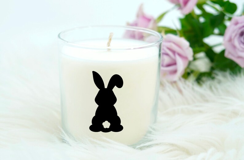 May include: A white candle in a clear glass jar with a black silhouette of a bunny rabbit on the front.