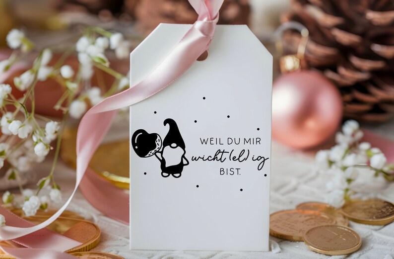 May include: White gift tag with a black and white illustration of a gnome holding a balloon. The tag has black text that reads "Weil du mir wichtig (el) ig bist."