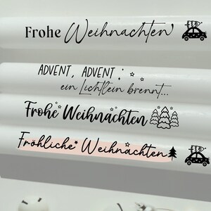 May include: Four white candles with black text and illustrations. The candles have the following text: "Frohe Weihnachten", "ADVENT, ADVENT, ein Lichtlein brennt...", "Frohe Weihnachten", and "Fr&ouml;hliche Weihnachten".