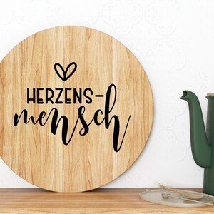 May include: A round wooden sign with the text "HERZENS-mensch" and a small heart symbol.