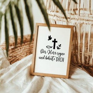May include: A wooden framed sign with a white background and black text. The text reads "Der Herr segne und beh&uuml;te DICH". There are also black icons of a dove, a fish, a cross, and an anchor.