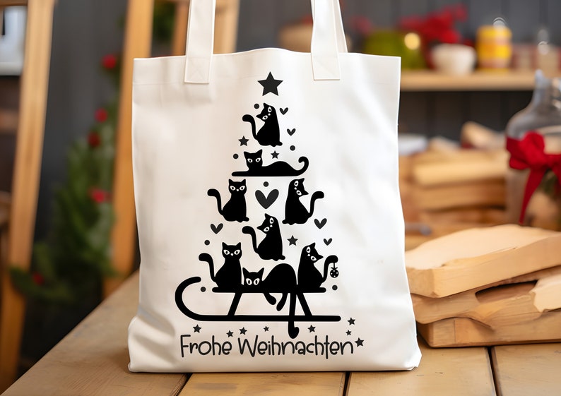 May include: White canvas tote bag with a black silhouette design of a Christmas tree made of cats. The text "Frohe Weihnachten" is printed at the bottom of the bag.