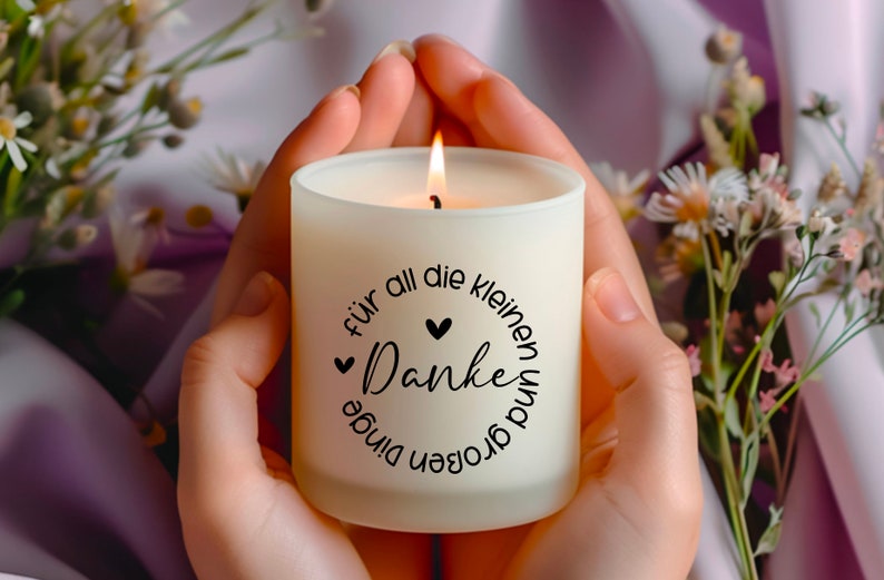 K&ouml;nnte beinhalten: Eine wei&szlig;e Kerze mit einem schwarzen Kreisdesign, auf dem "f&uuml;r all die kleinen und gro&szlig;en dinge Danke" mit zwei kleinen Herzen steht. Die Kerze ist angez&uuml;ndet und wird von den H&auml;nden einer Person gehalten.