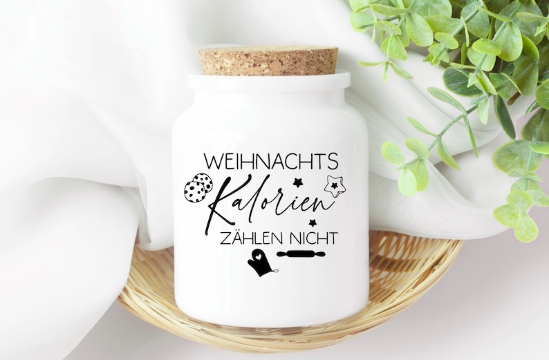 May include: White ceramic jar with a cork lid and a black and white design that says "Weihnachts Kalorien Z&auml;hlen Nicht". The jar is sitting on a woven basket.