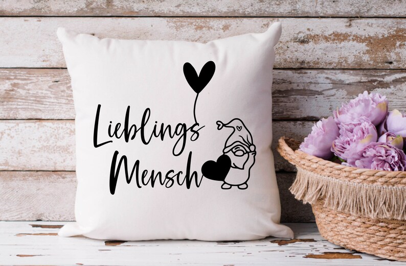 May include: White cushion with black text that reads "Lieblings Mensch" and a black and white illustration of a gnome holding a heart-shaped balloon.