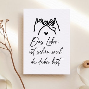 Puede incluir: Una tarjeta blanca con texto negro y un dibujo simple de dos manos haciendo una promesa con el me&ntilde;ique. El texto dice "Das Leben ist sch&ouml;n, weil du dabei bist." que se traduce como "La vida es hermosa porque est&aacute;s aqu&iacute;."
