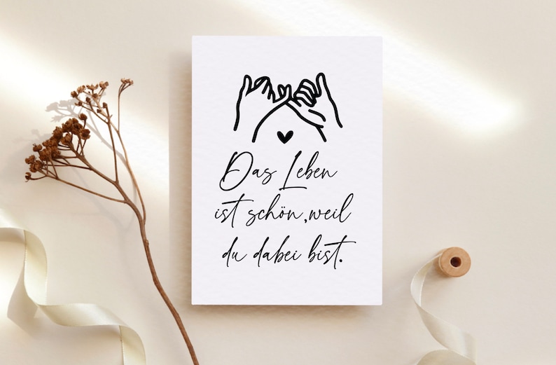 Puede incluir: Una tarjeta blanca con texto negro y un dibujo simple de dos manos haciendo una promesa con el me&ntilde;ique. El texto dice "Das Leben ist sch&ouml;n, weil du dabei bist." que se traduce como "La vida es hermosa porque est&aacute;s aqu&iacute;."