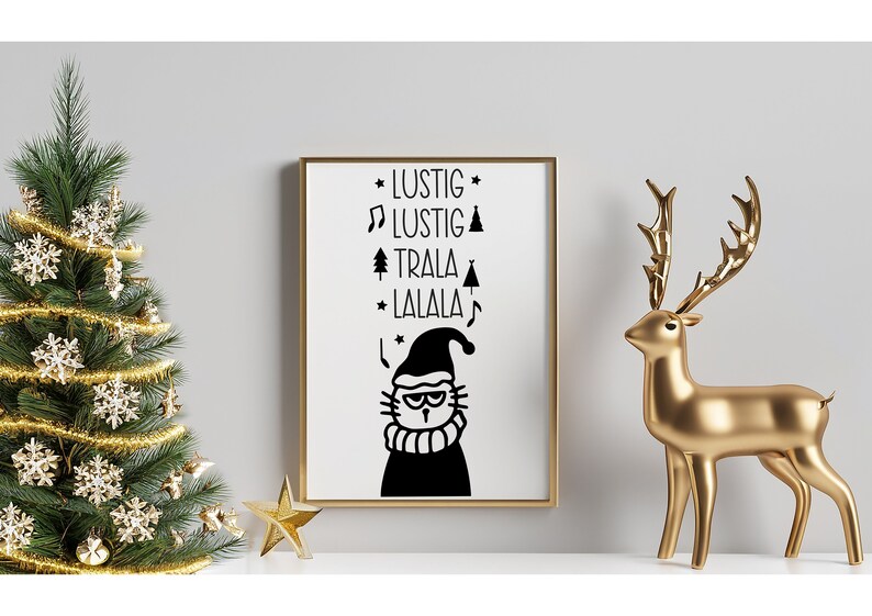 May include: A black and white printable art print with a cat wearing a Santa hat and the text "Lustig Lustig Trala Lalala". The print is framed in a gold frame and is displayed on a shelf with a gold reindeer figurine and a small Christmas tree.