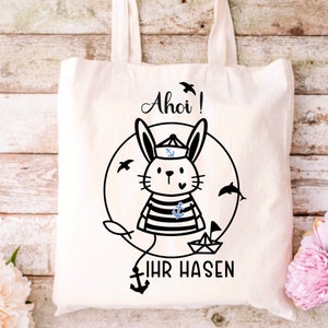 May include: A white tote bag with a black and white illustration of a bunny wearing a sailor hat and holding a small anchor. The text "Ahoi! Ihr Hasen" is printed below the bunny.