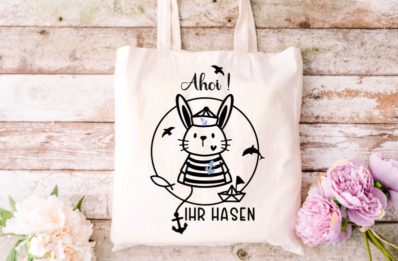 May include: A white tote bag with a black and white illustration of a bunny wearing a sailor hat and holding a small anchor. The text "Ahoi! Ihr Hasen" is printed below the bunny.