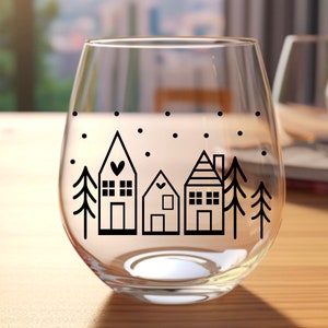 May include: A clear glass wine glass with a black and white design of a snowy village with three houses and two trees. The houses have small windows and doors, and the trees are simple silhouettes.