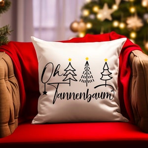 May include: White throw pillow with black text that reads "Oh Tannenbaum" and three stylized black Christmas trees with gold stars on top.