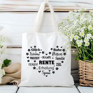 May include: White canvas tote bag with black text that reads "*Gl&uuml;ck* *Tr&auml;ume* *FREIZEIT* *HOBBY* *Spass* *Ruhe* *Reisen* *Kraft* *Familie* *RENTE* *Erholung* *ZIEL*" in a heart shape.