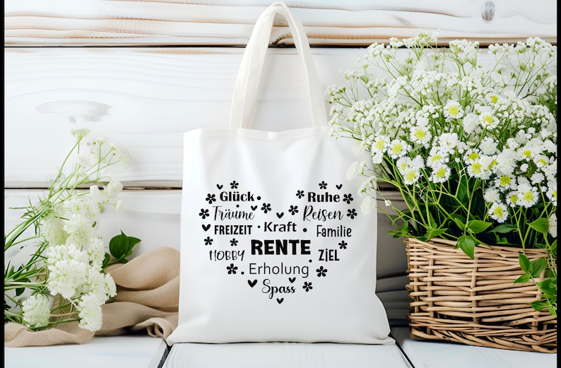 May include: White canvas tote bag with black text that reads "*Gl&uuml;ck* *Tr&auml;ume* *FREIZEIT* *HOBBY* *Spass* *Ruhe* *Reisen* *Kraft* *Familie* *RENTE* *Erholung* *ZIEL*" in a heart shape.