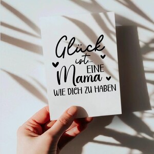 May include: A white card with black text that reads "Gl&uuml;ck ist... eine Mama wie dich zu haben". The card is decorated with small hearts.