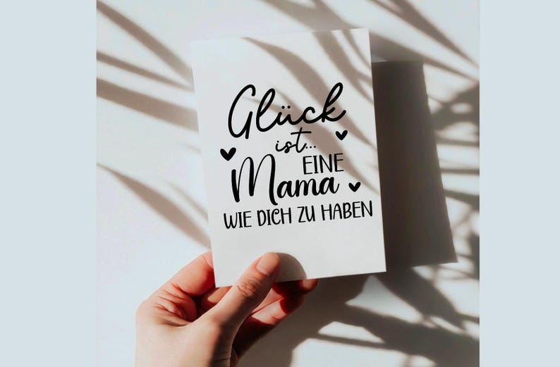 May include: A white card with black text that reads "Gl&uuml;ck ist... eine Mama wie dich zu haben". The card is decorated with small hearts.