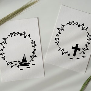 May include: Two black and white printable designs featuring a wreath with a boat and fish on one and a cross and fish on the other.