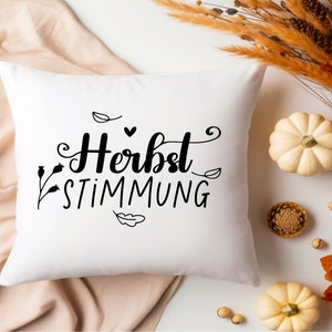 May include: White throw pillow with black text that reads "Herbst Stimmung" with a small heart and leaf designs.