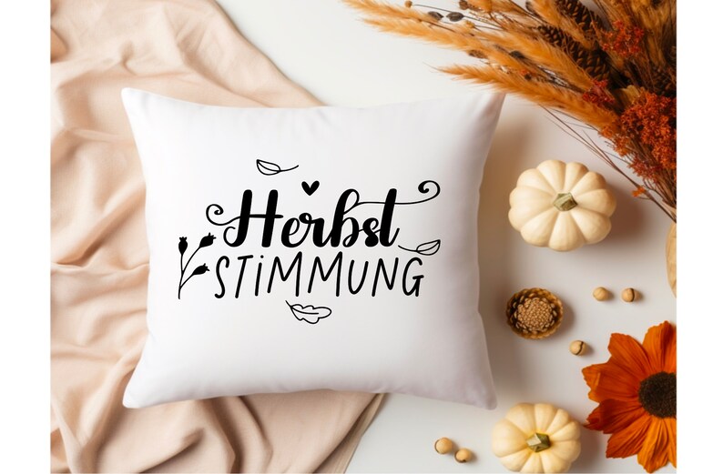 May include: White throw pillow with black text that reads "Herbst Stimmung" with a small heart and leaf designs.
