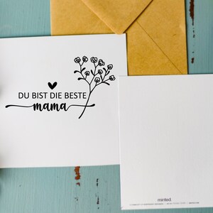 May include: A white card with black text and a small floral design. The text reads "Du bist die beste mama" which translates to "You are the best mom".