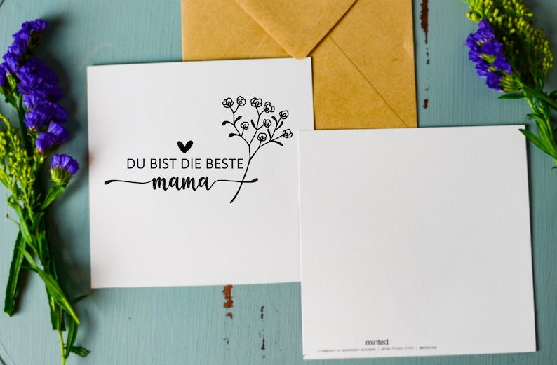May include: A white card with black text and a small floral design. The text reads "Du bist die beste mama" which translates to "You are the best mom".
