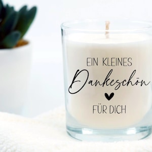 May include: A clear glass candle jar with a white candle inside. The candle has a black label with the text "Ein kleines Dankesch&ouml;n f&uuml;r dich" and a small black heart.
