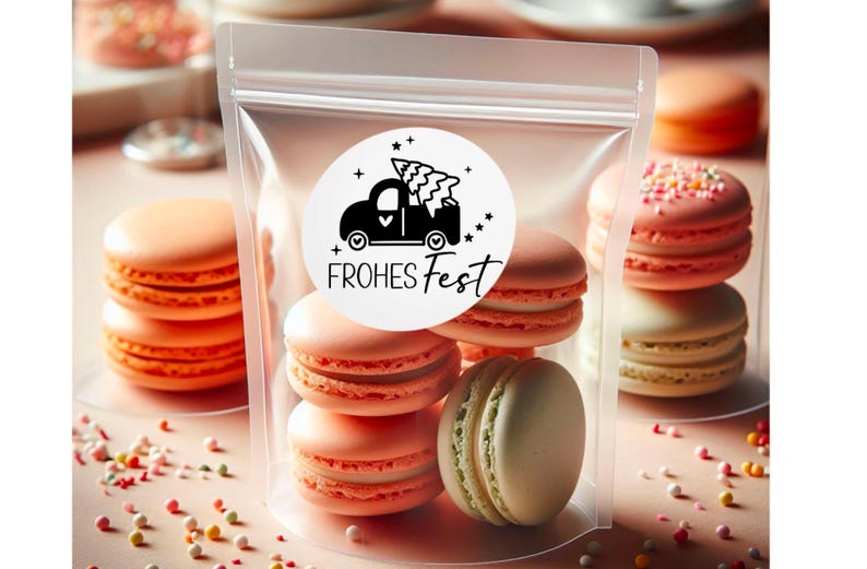 Puede incluir: Una bolsa de pl&aacute;stico transparente llena de macarons de color rosa pastel y verde. Una pegatina blanca con un cami&oacute;n negro que lleva un &aacute;rbol de Navidad y el texto "FROHES FEST" est&aacute; en la bolsa.