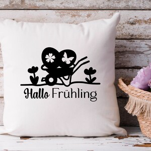 May include: White pillow with a black silhouette of a wheelbarrow carrying two hearts with flowers and butterflies. The text "Hallo Fr&uuml;hling" is below the wheelbarrow.