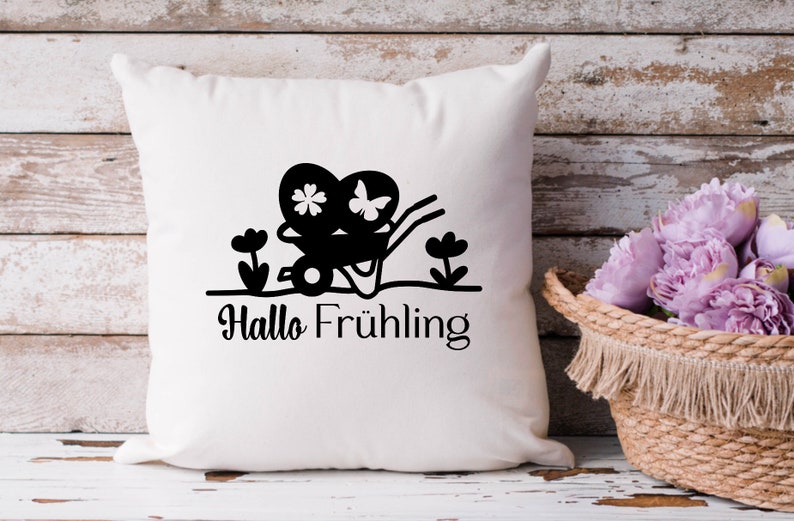 May include: White pillow with a black silhouette of a wheelbarrow carrying two hearts with flowers and butterflies. The text "Hallo Fr&uuml;hling" is below the wheelbarrow.
